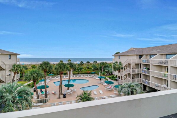 A hotel with a pool area, palm trees, and a view of the beach.