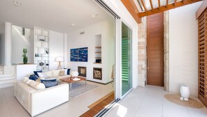 A modern living room with a sofa, coffee table, and fireplace. There is a sliding glass door leading to a stone wall and a wooden door.