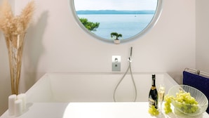 A bathroom with a bathtub, a round mirror, a potted plant, a bottle of champagne, and a bowl of grapes.