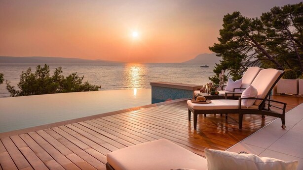 An infinity pool with lounge chairs and a sunset view.