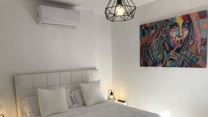 A neatly made bed with white linens, a geometric pendant light, and a colorful abstract painting on the wall. - Home SEA & DREAMS OldTown I (Calp)