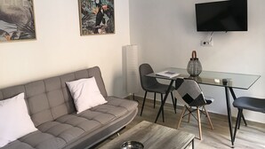 A modern living room with a grey sofa, a glass coffee table, a dining table with chairs, and a flat-screen TV mounted on the wall. - Home SEA & DREAMS OldTown I (Calp)