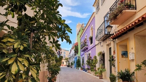 A narrow street lined with colorful buildings, potted plants, and balconies with railings. - Home SEA & DREAMS OldTown I (Calp)