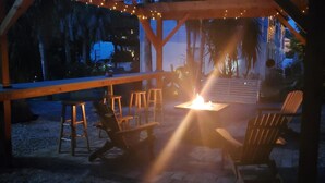 An outdoor seating area with wooden chairs and a table under a wooden pergola, with string lights above.