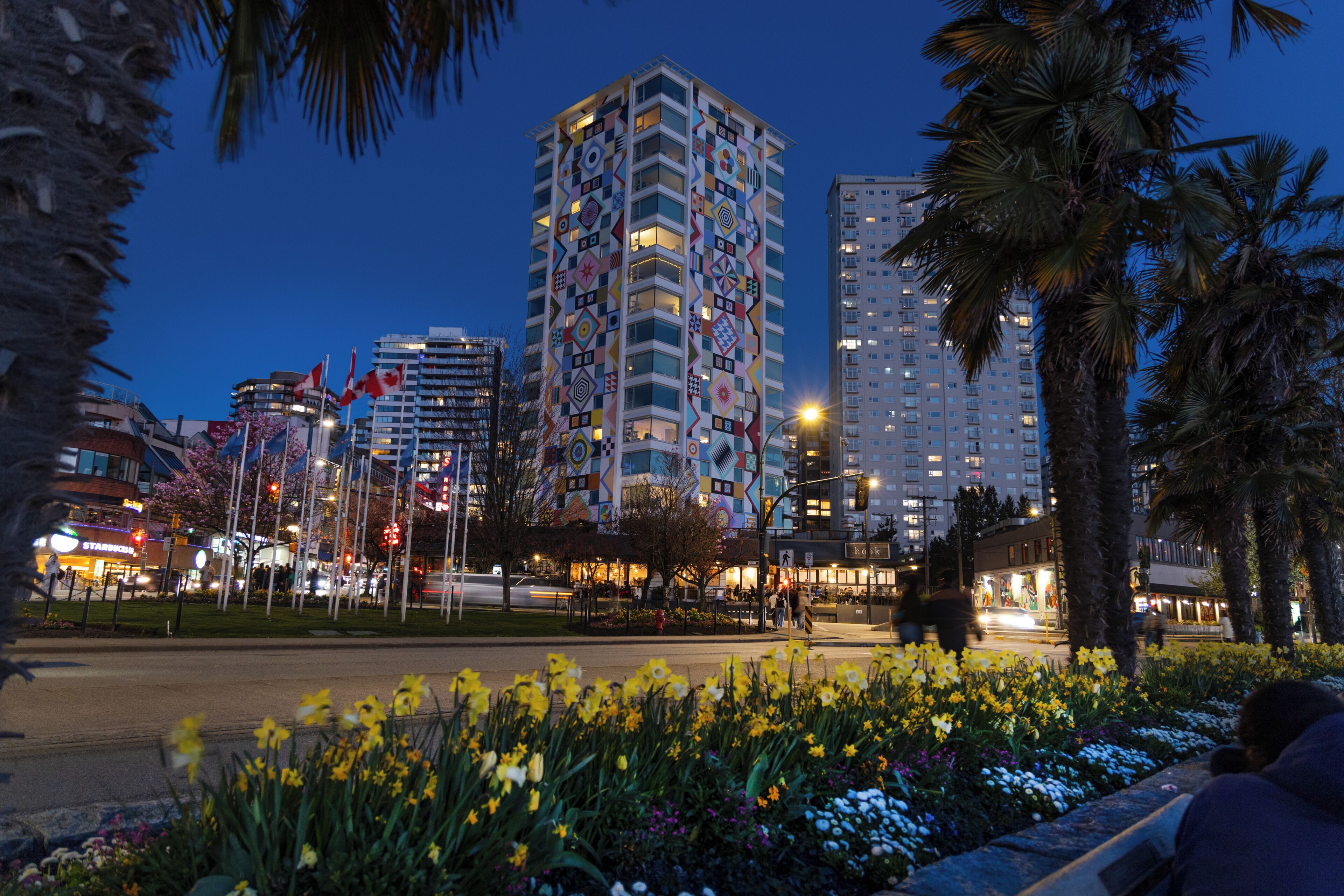 Un paisaje urbano al anochecer con edificios altos, incluyendo uno con patrones geométricos de colores.