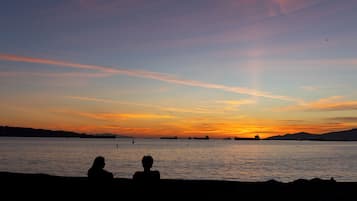 Silhuetas de duas pessoas sentadas à beira da água durante o pôr do sol.
