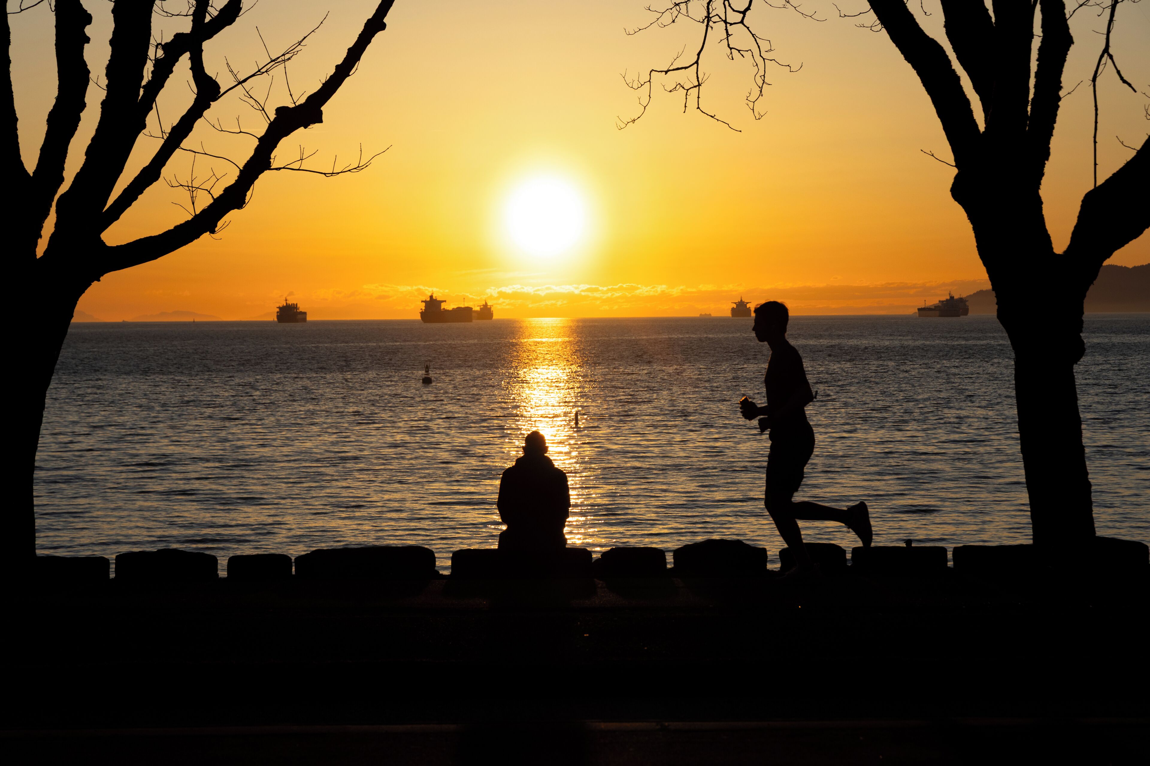 A sunset over water with silhouettes of people and ships.