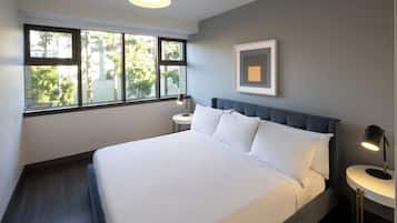 Una habitación de hotel moderna con una cama grande, una mesita de noche y una ventana con vistas a árboles.