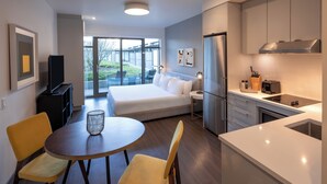 A modern hotel room with a bed, a dining area with a table and chairs, a kitchen with a refrigerator and stove, and a sliding glass door to the outside. - Revival English Bay, Vancouver  (Vancouver)