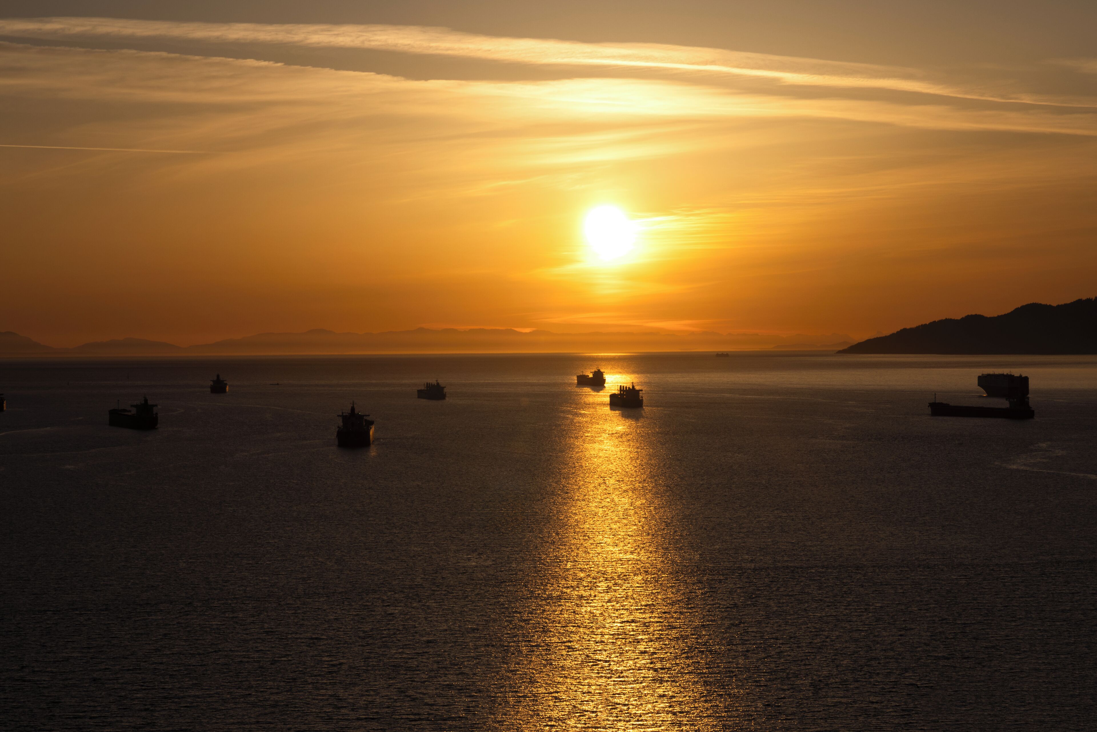 Un coucher de soleil sur une mer calme, avec plusieurs navires à l'horizon.