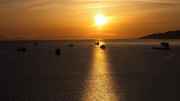 Un coucher de soleil sur une mer calme, avec plusieurs navires à l'horizon.