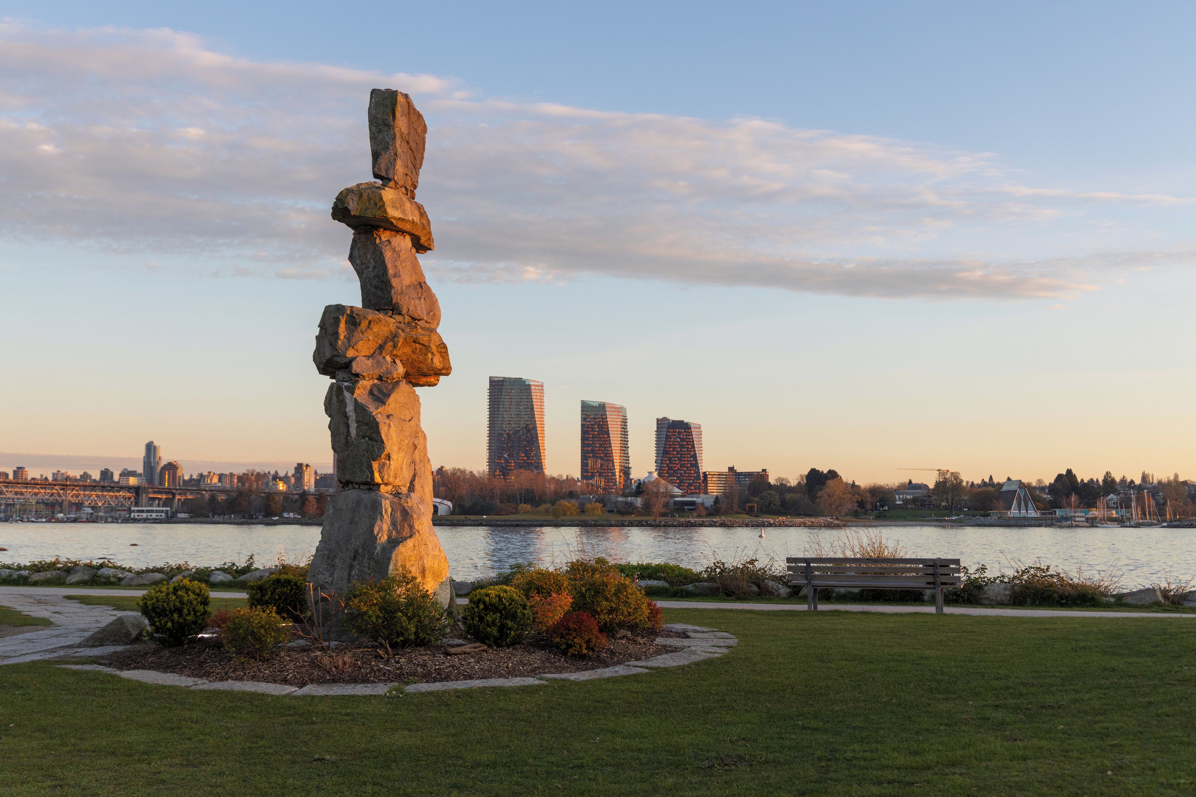 Une grande sculpture en pierre dans un parc, avec la silhouette de la ville en arrière-plan.
