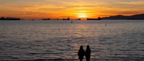 A sunset over a body of water with ships and silhouettes of people.