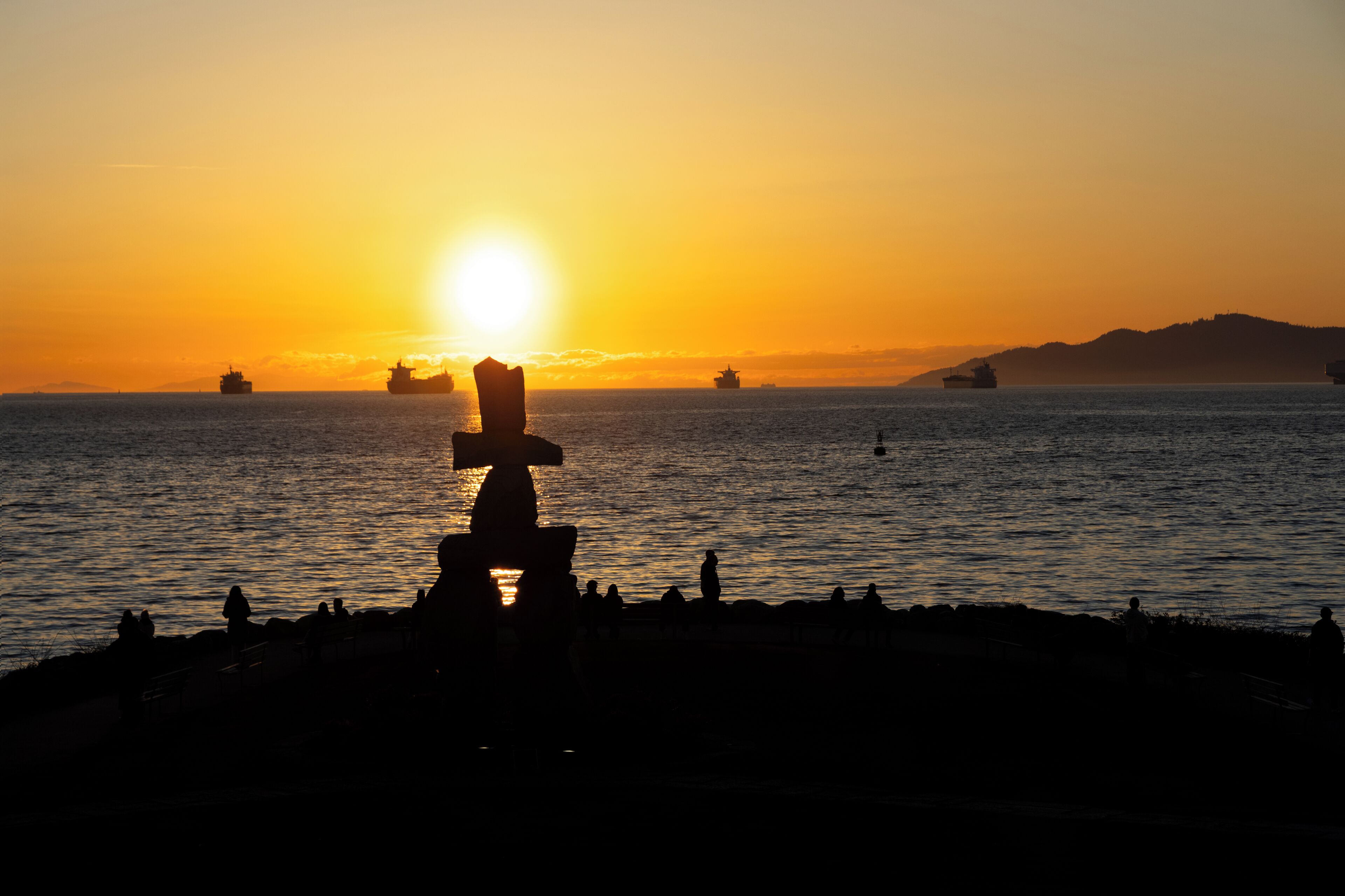 Un atardecer sobre una masa de agua, con barcos a lo lejos y la silueta de un tótem.