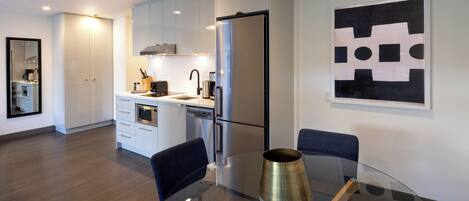 Una cocina moderna con armarios blancos, un refrigerador de acero inoxidable y una mesa de vidrio con sillas.