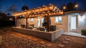 Ein überdachter Außenbereich mit Pergola, Steinstufen und einer Terrasse.