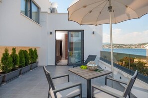 Uma varanda com mesa, cadeiras, um guarda-sol e vista para o mar.