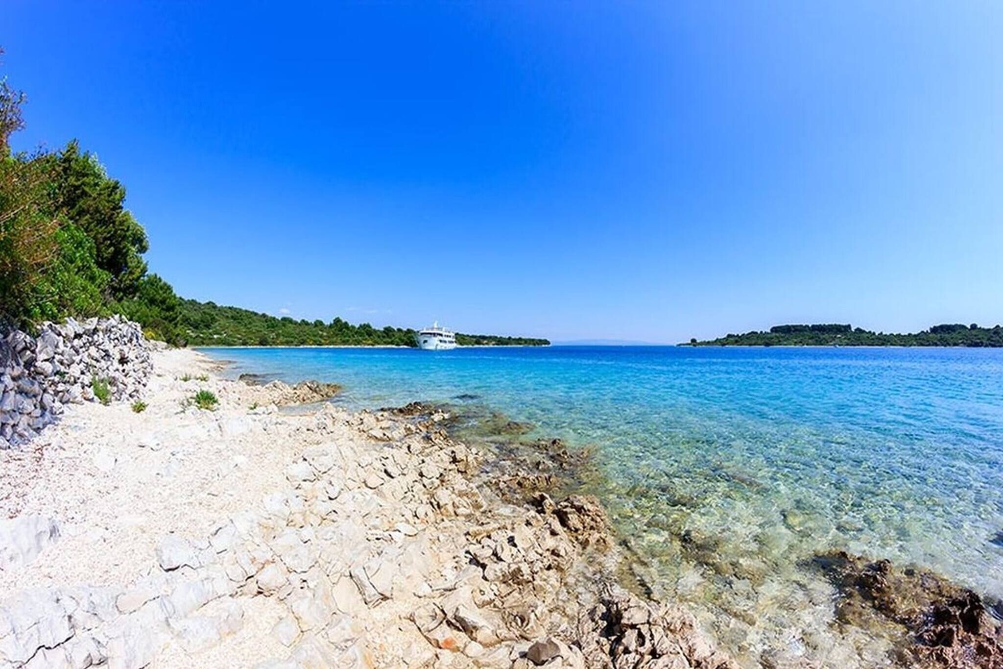 Une plage rocheuse aux eaux cristallines, un bateau et des îles qui se dessinent à l’horizon.