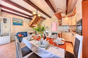 Un comedor con una mesa dispuesta para cuatro personas, una escalera y una cocina al fondo.