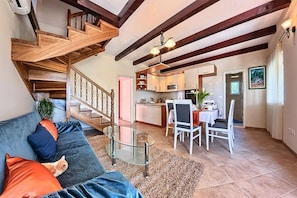 Una sala de estar con un sofá, una mesa de centro de vidrio, un comedor con sillas, una cocina y una escalera de madera.