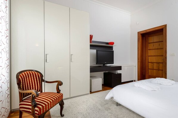 Quarto de hotel com cama, guarda-roupa de madeira, televisão e uma cadeira.