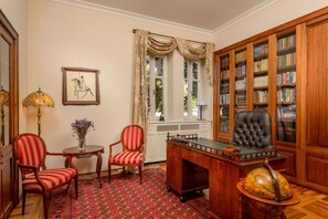 A room with a wooden desk, two chairs, a globe, a bookshelf, and a window with curtains.