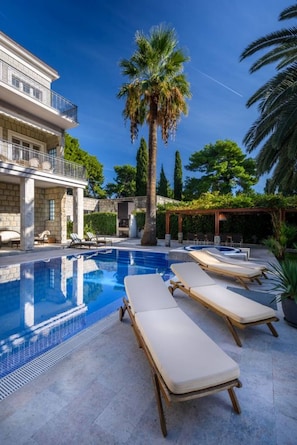 A swimming pool with lounge chairs, a palm tree, and a building with a balcony.