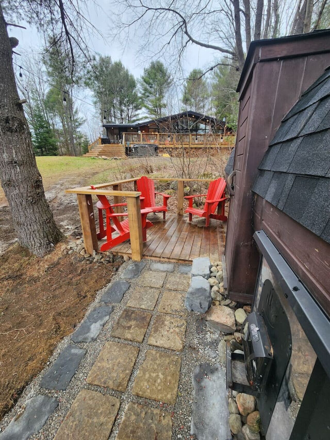A deck with red Adirondack chairs, a stone pathway, and a wood-burning stove.
