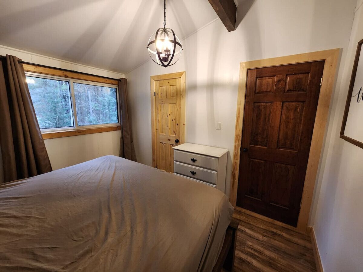 A bedroom with a bed, a nightstand, a dresser, a wooden door, and a window with curtains.