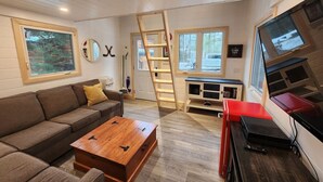 Una sala de estar acogedora con una mesa de centro de madera, un sofá, un televisor y una escalera que lleva a una zona superior.