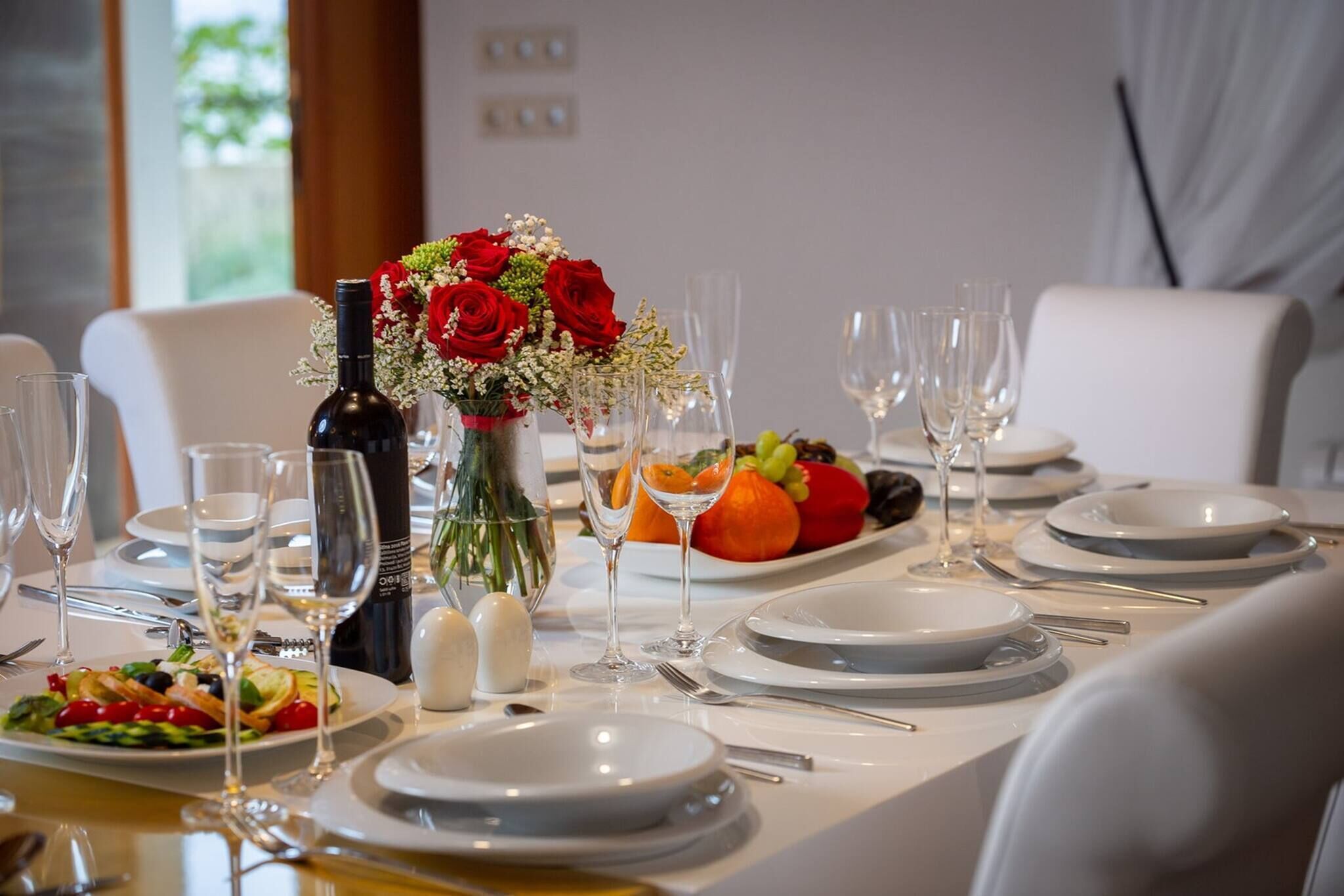 A dining table set with plates, glasses, cutlery, a bottle, and a floral centerpiece.