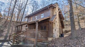 Eine Blockhütte mit einer Holztreppe, die zu einer Terrasse führt, umgeben von Bäumen.