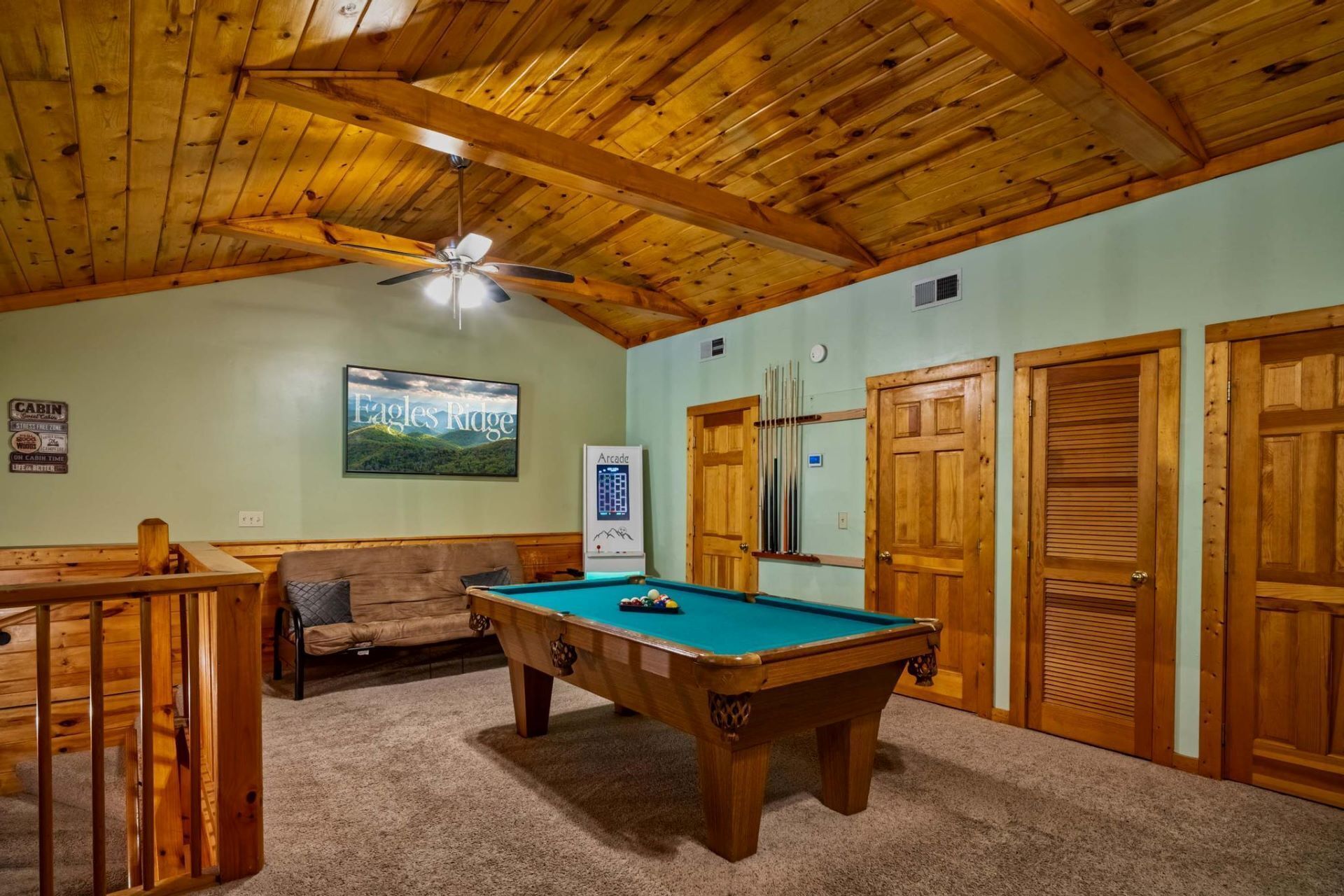 A pool table in a room with wooden ceiling beams, a couch, and a framed picture on the wall.