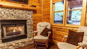 Ein gemütliches Blockhaus-Interieur mit Kamin aus Stein, Holzwänden und zwei Schaukelstühlen.