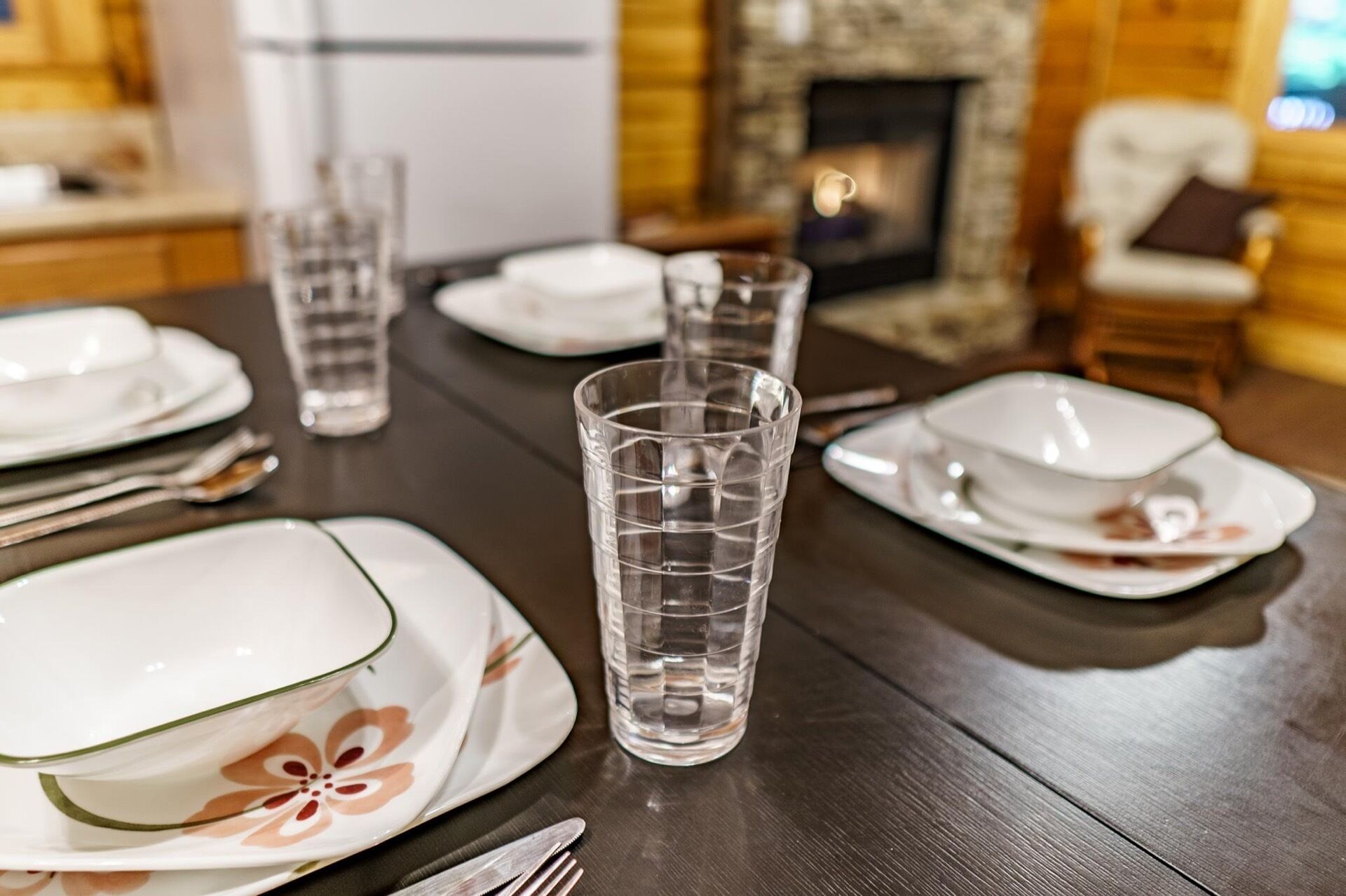 A dining table set with plates, glasses, and cutlery, with a fireplace in the background.
