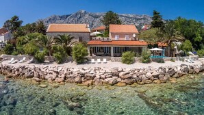 A coastal hotel with a clear view of the sea, a stone wall, and a mountain in the background.