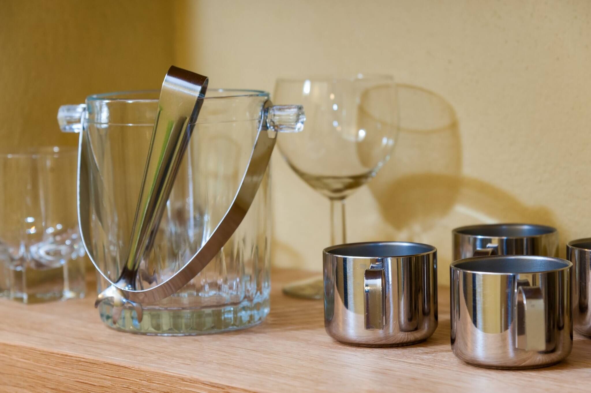 A clear glass pitcher with a metal handle, a glass carafe, and several metal cups on a wooden surface.