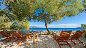 A beachside seating area with wooden chairs and a table, overlooking a clear blue sea. - Luxury Seafront Villa Mare Orebic with Pool (Orebic)