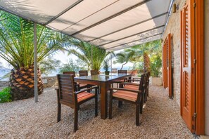 Ein Essbereich im Freien mit Tisch und Stühlen, umgeben von Palmen und Blick aufs Meer.