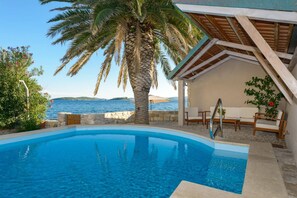 A swimming pool with a view of the sea, a palm tree, and a covered seating area. - Luxury Seafront Villa Mare Orebic with Pool (Orebic)