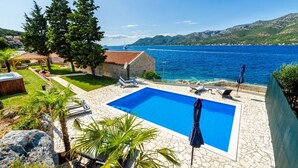 A swimming pool with lounge chairs and umbrellas, surrounded by greenery and a view of the sea. - Luxury Seafront Villa Gabriela with Pool And Gym (Korcula)
