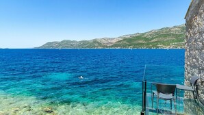 A clear view of the sea with a person swimming, a glass balustrade, and a stone building. - Luxury Seafront Villa Gabriela with Pool And Gym (Korcula)