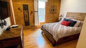 A bedroom with a wooden floor, a bed with pillows, a ceiling fan, a window with curtains, and a wall-mounted TV. - Lakeview Loft (Kewaunee)