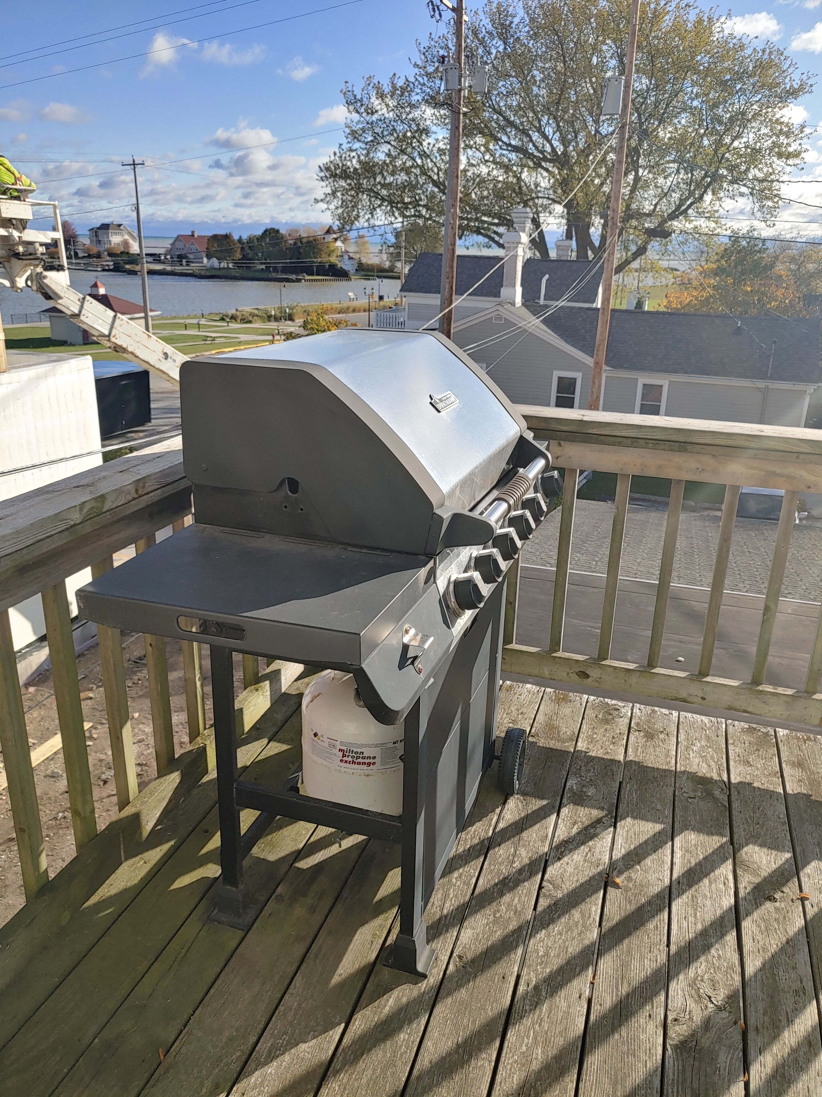 A barbecue grill on a wooden deck with a view of a lake and houses in the background.