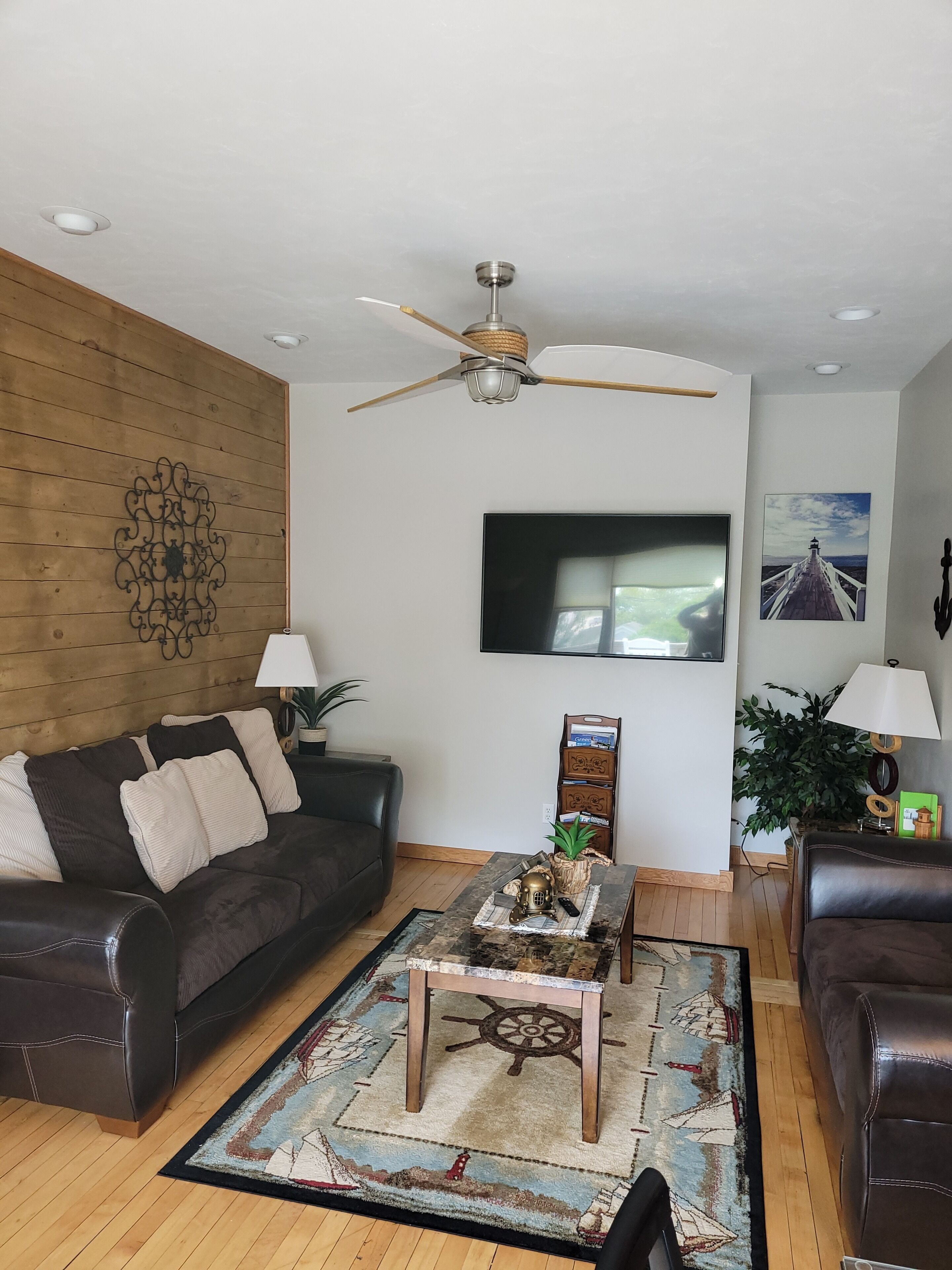 Ein Wohnzimmer mit Deckenventilator, Flachbildfernseher, Holzwand, gemustertem Teppich und einer Ledersofa.