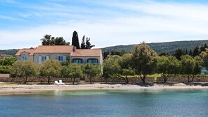 A coastal property with a stone wall, a beach, and a house with a tiled roof. - Luxury Seafront Villa Casa Mare Brač Heated Pool (Supetar)