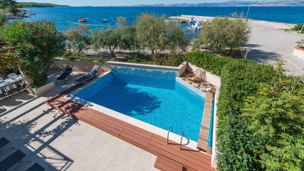 A swimming pool with a view of the sea, surrounded by greenery and a deck area. - Luxury Seafront Villa Casa Mare Brač Heated Pool (Supetar)
