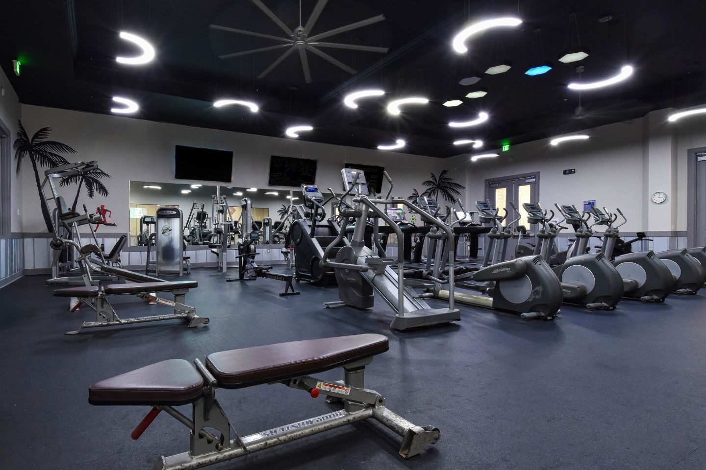 Een sportschool met diverse fitnessapparaten, waaronder loopbanden, hometrainers en krachtapparaten.