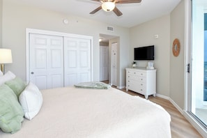 Un dormitorio con cama, cómoda, televisor y puerta que da a otra habitación.