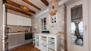 Une cuisine aux murs en pierre, avec un plafond en bois et une vue sur la mer par une porte.